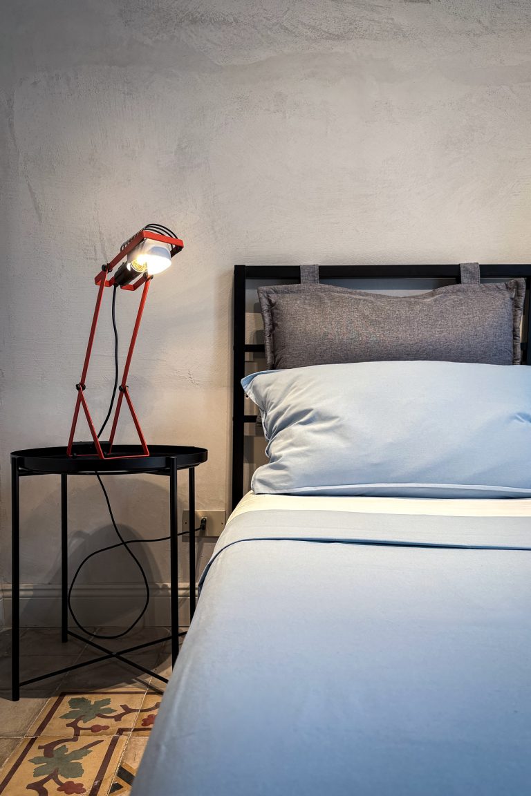 Modern bedroom at Feelgood Sicily holiday home in Ispica, Italy, with minimalist bedside table and red designer lamp.