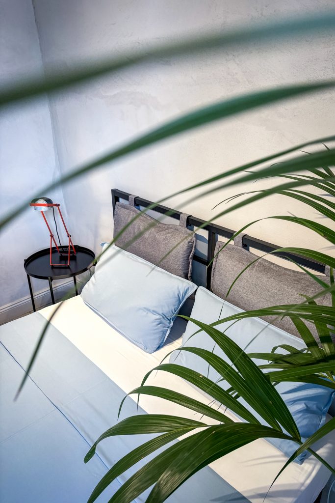 Stylish bedroom with black metal bed frame, red bedside lamp and tropical plant at Feelgood Sicily holiday home in Ispica, Italy.