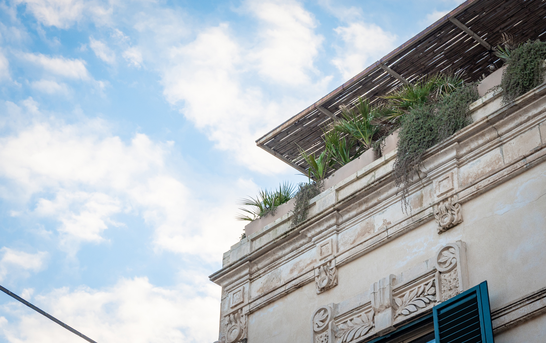 Historic Sicilian townhouse facade with rooftop terrace and Mediterranean plants under blue sky at Feelgood Sicily holiday home in Ispica, Italy.