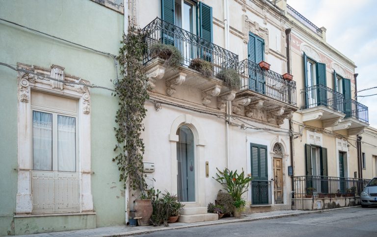 Street view of historic townhouse facade with balconies and green shutters, home to Feelgood Sicily holiday house in Ispica, Italy.