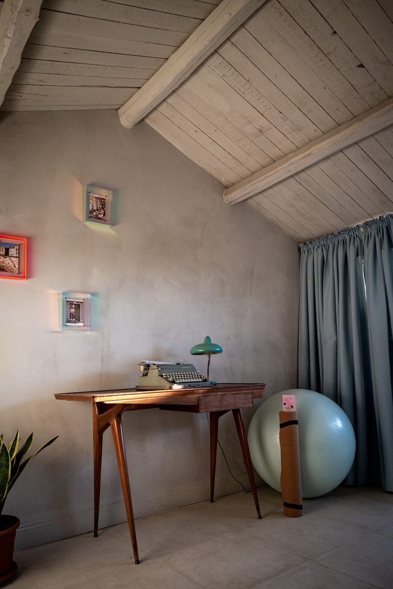Cozy attic workspace with vintage wooden desk, retro typewriter and green desk lamp under white wooden ceiling at Feelgood Sicily holiday home in Ispica, Italy.