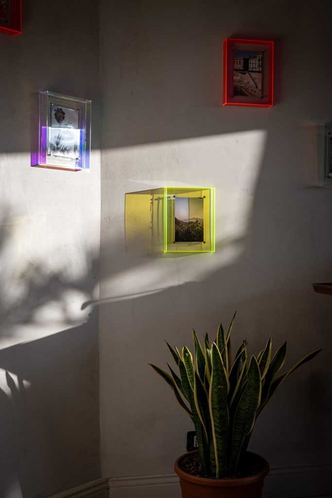 Close-up of colorful framed wall art with sunlight and potted plant in a stylish attic interior at Feelgood Sicily holiday home in Ispica, Italy.