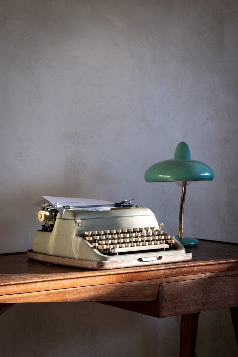 Vintage typewriter and green desk lamp on a wooden desk in a sunlit attic room at Feelgood Sicily holiday home in Ispica, Italy.