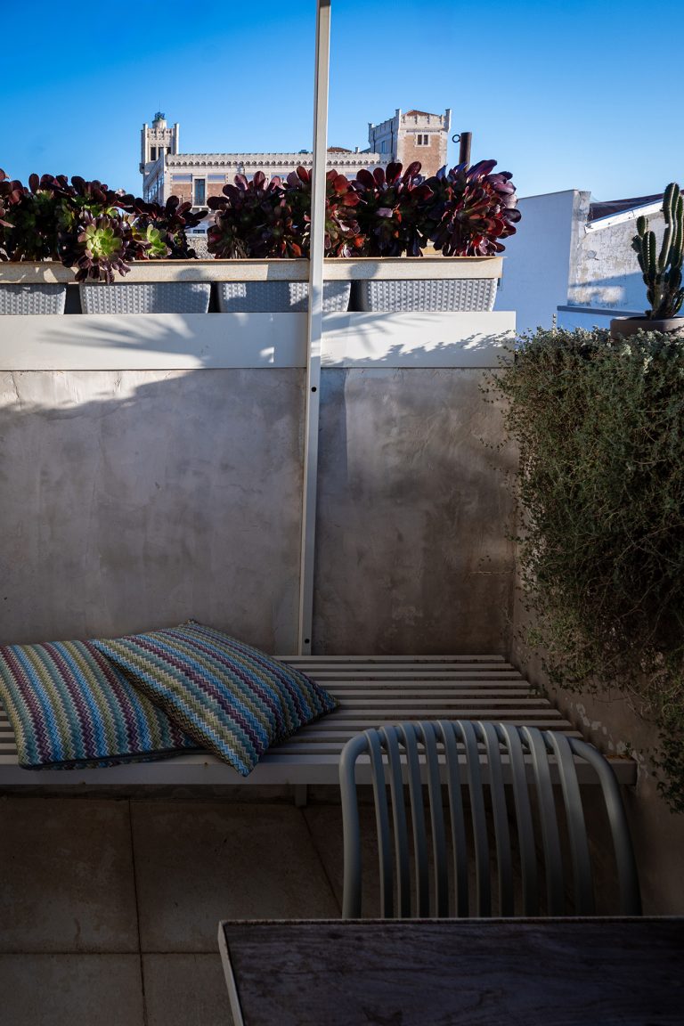 Rooftop terrace with built-in bench, patterned cushions and Mediterranean plants overlooking historic buildings in Ispica at Feelgood Sicily holiday home, Italy.