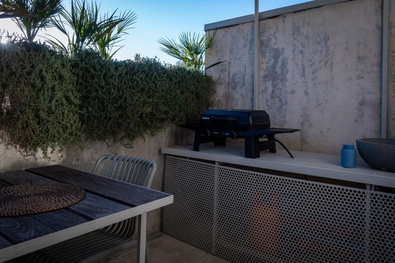 Rooftop terrace with outdoor dining table and gas barbecue surrounded by Mediterranean plants at Feelgood Sicily holiday home in Ispica, Italy.